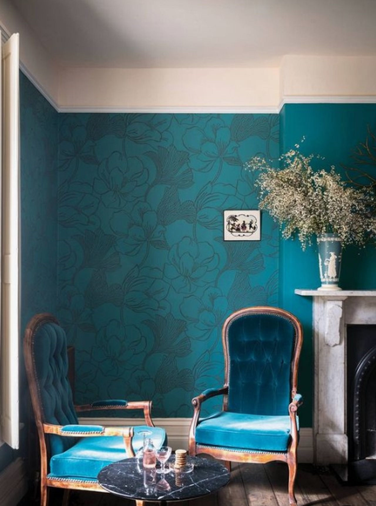 Phòng khách tinh tế được thực hiện trong sắc thái đậm của màu xanh, với đồ nội thất trang nhã, lò sưởi bằng đá cẩm thạch và bàn cà phê.