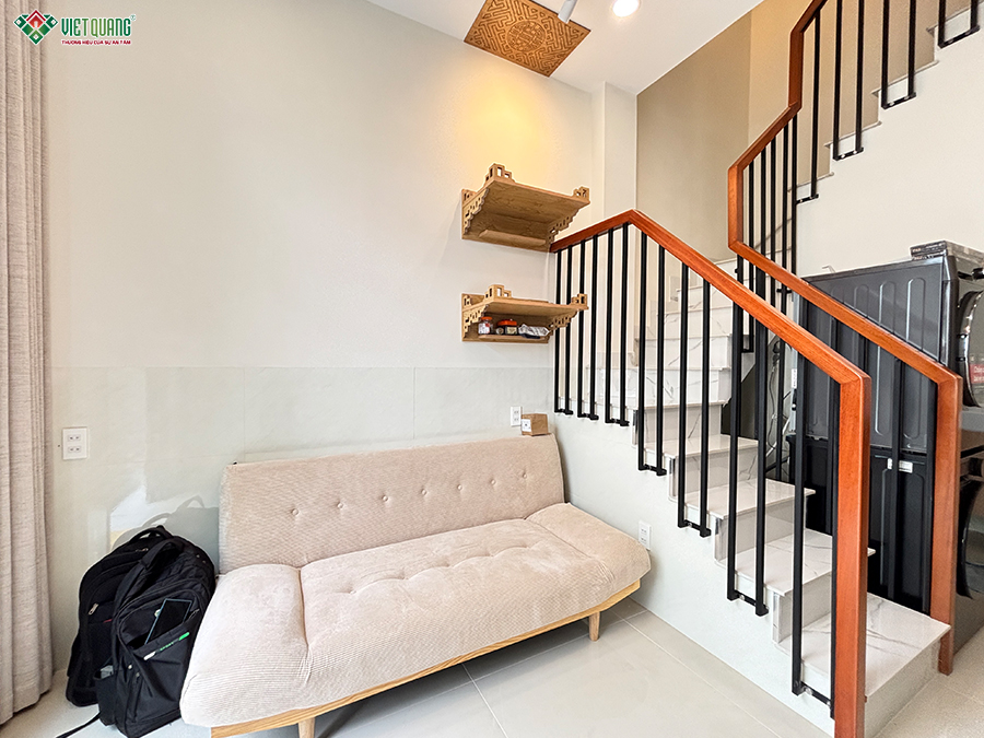 Không gian bên trong được hoàn thiện theo hướng gọn và tận dụng diện tíchBước vào bên trong, cách tổ chức không gian cho thấy ưu tiên rõ ràng về khả năng sử dụng thực tế. Các khu vực được bố trí vừa đủ, hạn chế những chi tiết chiếm nhiều diện tích và sử dụng gam màu sáng để tạo cảm giác rộng hơn so với kích thước thực tế. Khu vực cầu thang được bố trí sát một bên nhà với bậc hoàn thiện màu sáng, hệ lan can thanh sắt đen kết hợp tay vịn gỗ. Cách xử lý này vừa đảm bảo giao thông giữa các tầng vừa giữ được độ thoáng về thị giác. Phần diện tích liền kề cầu thang tiếp tục được tận dụng cho các nhu cầu sinh hoạt thay vì trở thành khoảng trống khó sử dụng. Màu trắng và màu gỗ xuất hiện xuyên suốt trong nhiều không gian, từ cửa, tủ, giường đến các chi tiết trang trí. Đây cũng là cách tạo sự liên kết giữa các khu vực trong một ngôi nhà có diện tích không quá lớn.